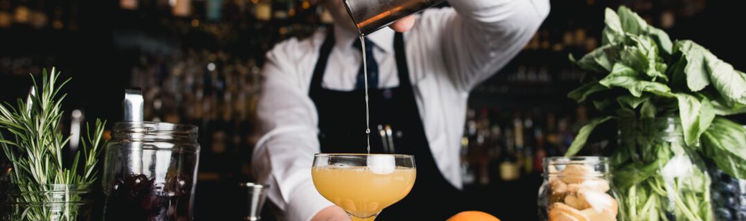 Barkeeper der einen Drink in ein Glas fliesen lässt