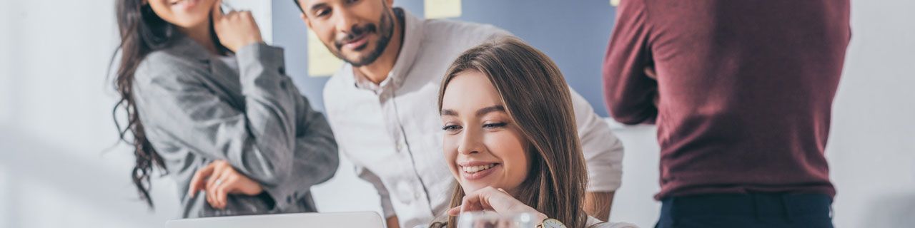 Gruppe Menschen blicken lächelnd auf einen PC